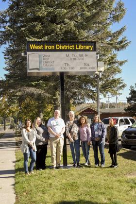 Library staff stand under the new electronic sign for the West Iron District Library.