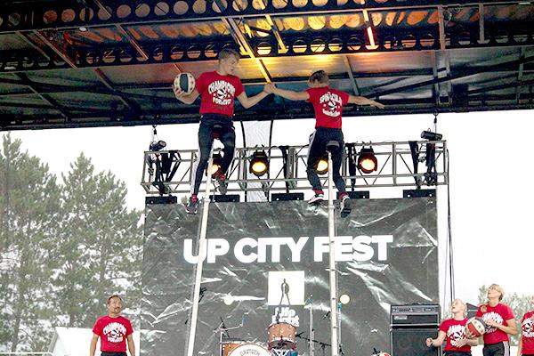 A pair of unicyclists performing an act in front of a banner for the U.P. City Fest.