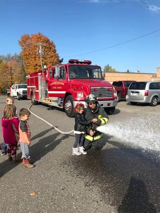 A member of the Caspian-Gaastra Fire department gives a hands-on demonstration to one of Denise Maloney's pre-K students on how to handle and spray a fire hose.