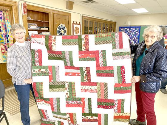 Karen Ivens (left) and Carol Erickson display a Christmas quilt at the Carrie Jacobs-Bond Quilters club. Each quilt is sewn from hundreds of pieces of material. The club has been established since 1985 and consists of 39 members. (photo by Kate Collins)